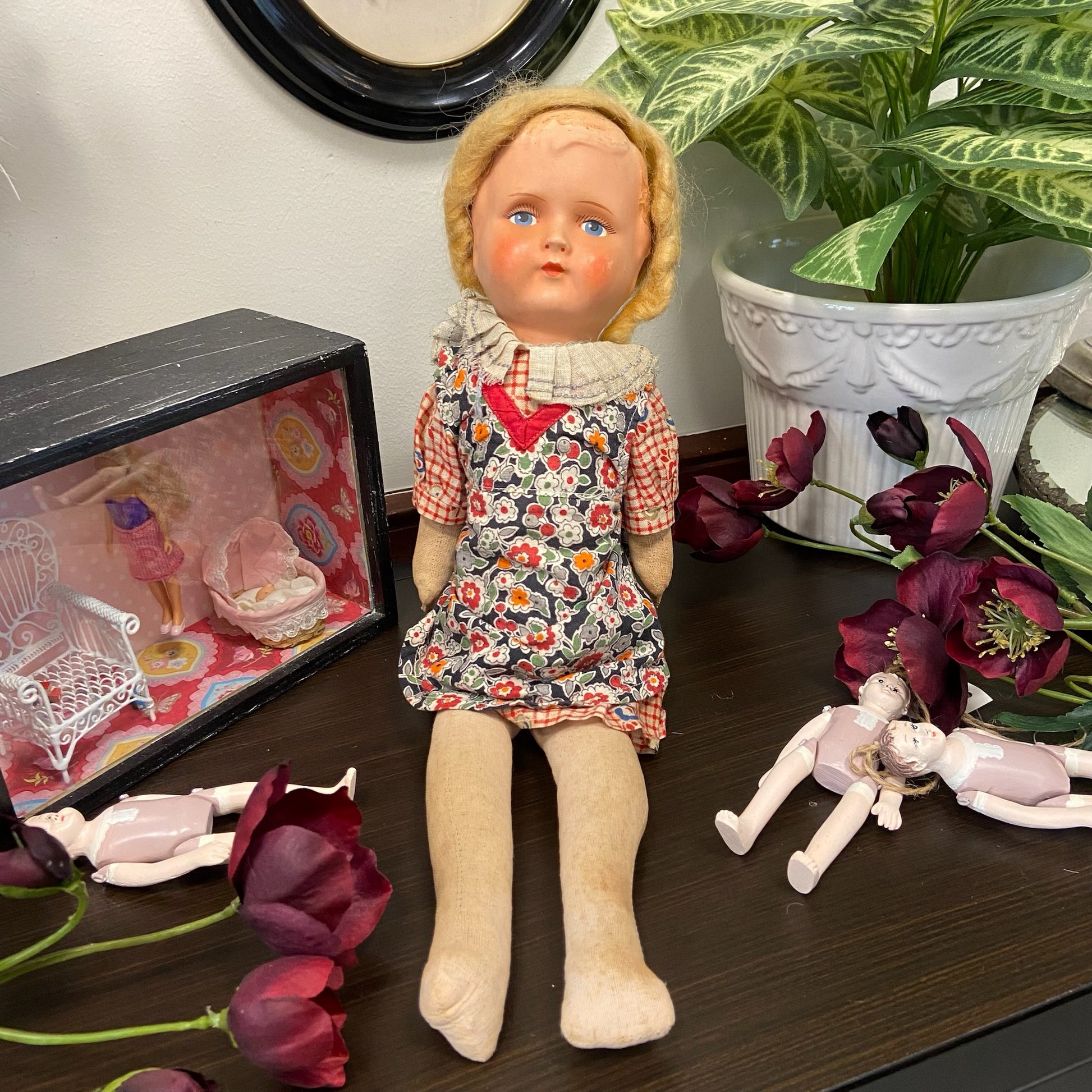 Docka med rutig klänning och blommigt förkläde. Huvud av celluloid och stoppad kropp i textil.