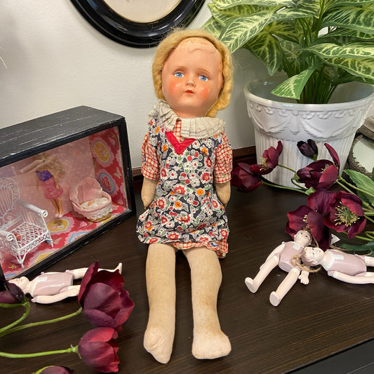 Docka med rutig klänning och blommigt förkläde. Huvud av celluloid och stoppad kropp i textil.