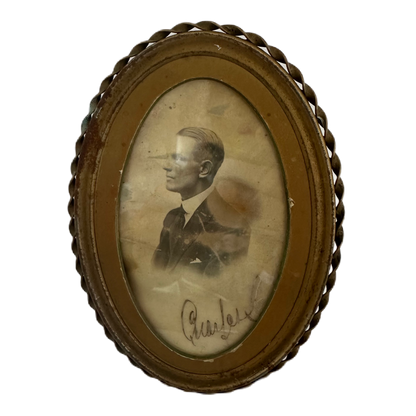 Oval, mässingsfärgad tavla med patina innehållande ett fotografi på en man från svunna tider.