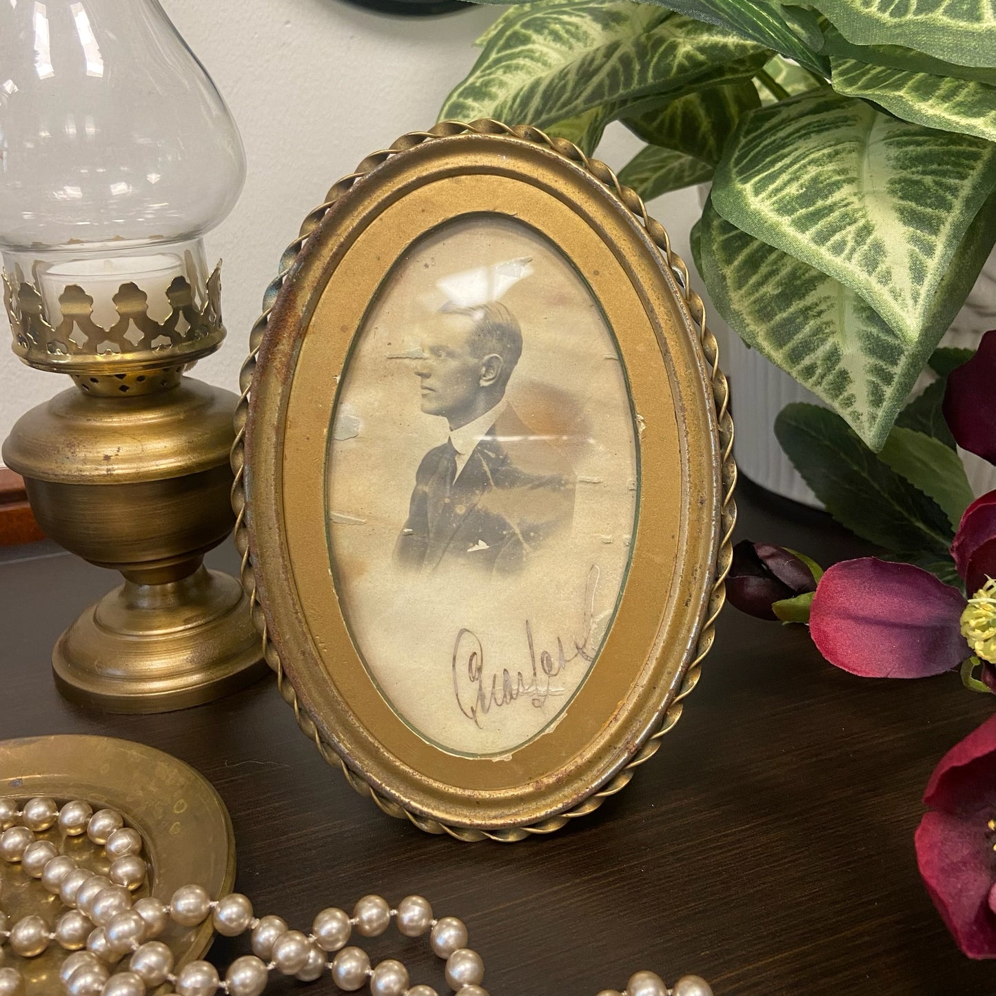 Oval, mässingsfärgad tavla med patina innehållande ett fotografi på en man från svunna tider.