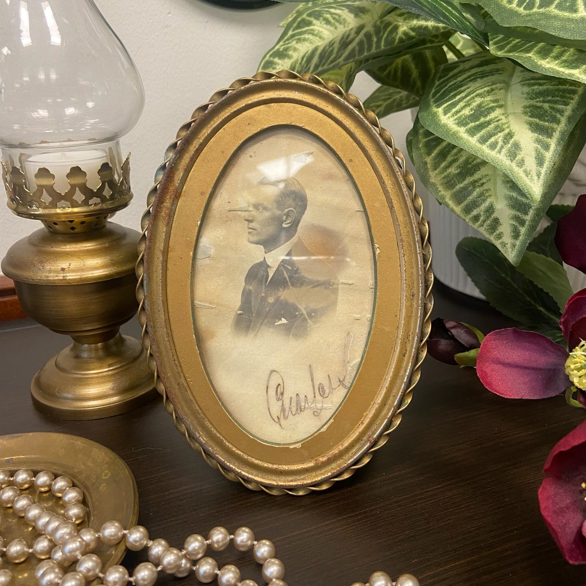 Oval, mässingsfärgad tavla med patina innehållande ett fotografi på en man från svunna tider.